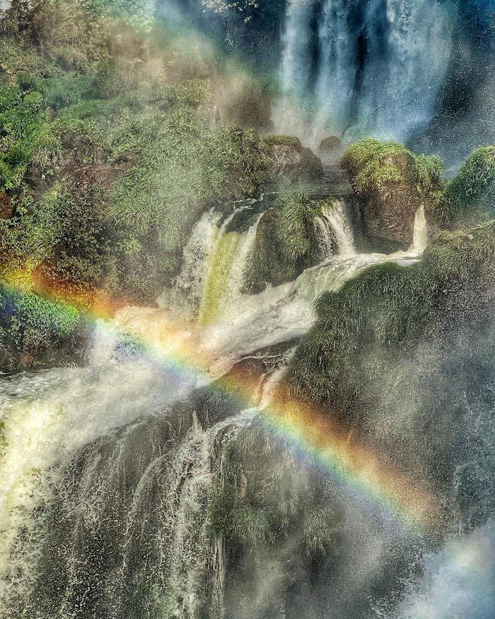 A stunning aerial view of Iguazu Falls in Argentina, showcasing a vibrant rainbow amidst lush greenery and cascading waters.